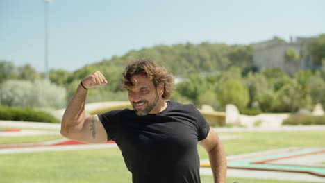 Medium-shot-of-happy-sportsman-showing-biceps-muscles-in-park